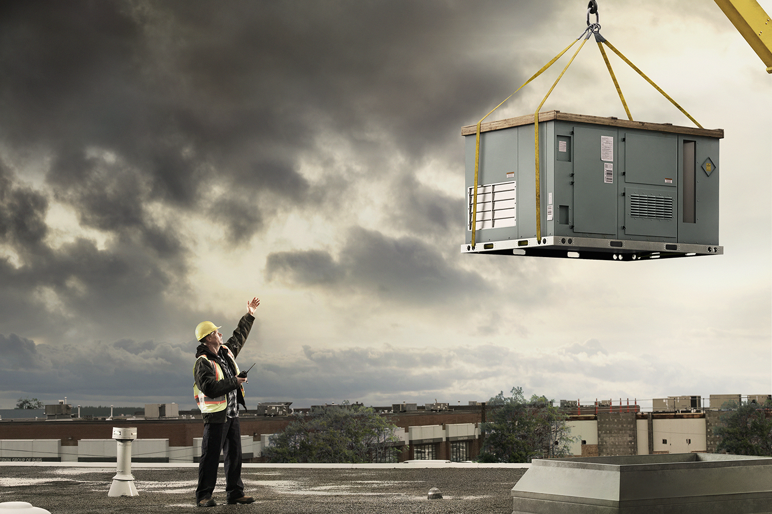 man directing crane to position a rooftop unit onto the roof of a building