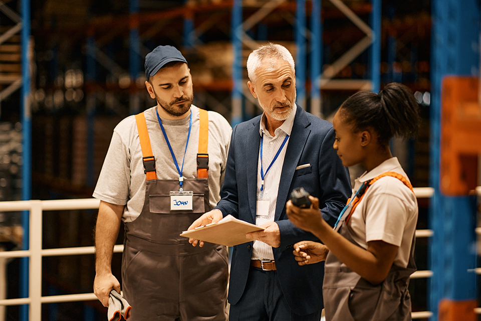 Young workers communicating with senior inspector at distribution warehouse