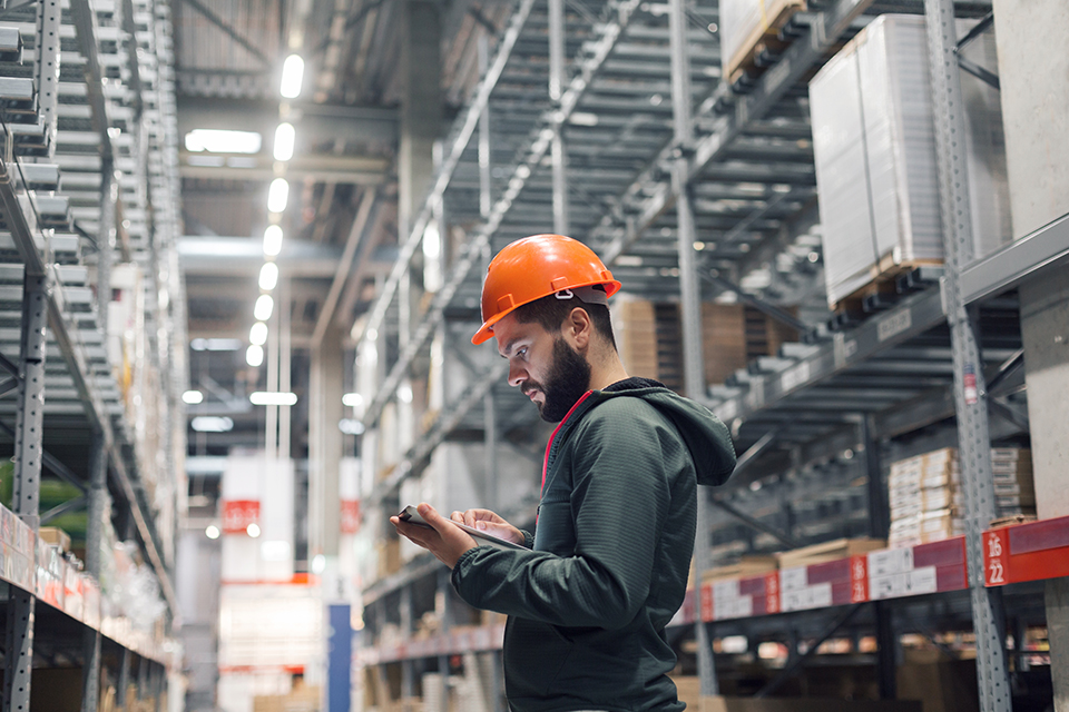 warehouse worker wearing hard hat while using an electronic tablet